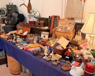 Packed table of vintage collectibles — electric fans, tins, framed art & cast-iron stove