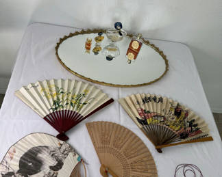 Lot 79: Oval gilt-mild mirror with vintage perfume bottles and decorative folding fans