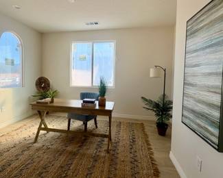 Wood campaign style desk, sisal rug, floor lamp, blue chair, large abstract wall art, faux plants