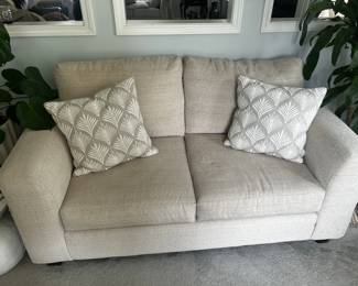 Cream Bouclé-Style Loveseat Description: Comfortable cream-colored loveseat upholstered in a soft textured fabric. Features wide track arms, deep seat cushions, and two coordinating decorative accent pillows. Neutral color palette makes it easy to incorporate into a variety of décor styles. Ideal for a living room, office, den, or apartment. Estate Sale Price: 175$