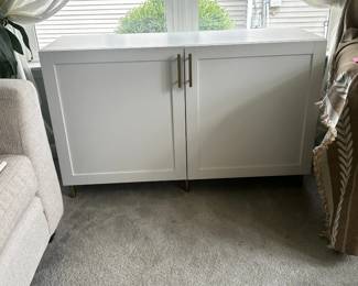 White Modern Storage Cabinet / Sideboard Description: Clean-lined white storage cabinet with contemporary shaker-style doors, brushed gold-tone hardware, and slim metal legs. Offers concealed storage behind two doors, making it perfect as a buffet, entryway cabinet, media console, or accent piece. Neutral design complements modern, transitional, and farmhouse décor. Price: $125