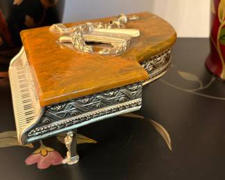 The Thorens grand piano music box features a butterscotch colored bakelite lid and a raised musical emblem. Base is gold gilt metal and raised design. Swiss movement