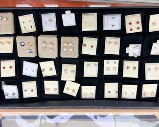 Multiple pairs of pearl studs on 14K gold cards. Several small diamond or diamond-like studs. Red gemstone studs (possibly garnet, ruby, or synthetic stones). Gray pearl studs. Butterfly/motif earrings. A few loose charms or pins mixed in.