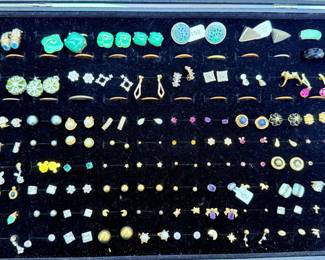 Multiple faux pearl studs. Cubic zirconia (CZ) stud earrings in various sizes. Green stone earrings (possibly dyed quartz, glass, jade simulant, or resin). Blue enamel and gold-tone earrings. Purple stone earrings. Several novelty designs (stars, moons, animals, flowers). Some vintage-style clip-on earrings.