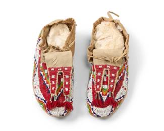 1355 A pair of Sioux beaded hide moccasins Early 20th century; Northern/Central Plains Each with polychrome beaded geometric motifs and tin cone and thread accents 2 pieces Each: 10.25" L x 4.25" W Estimate: $400 - $600