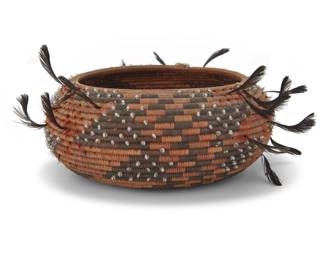 1232 A Pomo beaded gift basket Early 20th century; Central California The coiled basket rim mounted with shell disc beads, the body adorned with quail topknots and glass beads, finely woven with serrated columns 2" H x 5" Dia. Estimate: $800 - $1,200