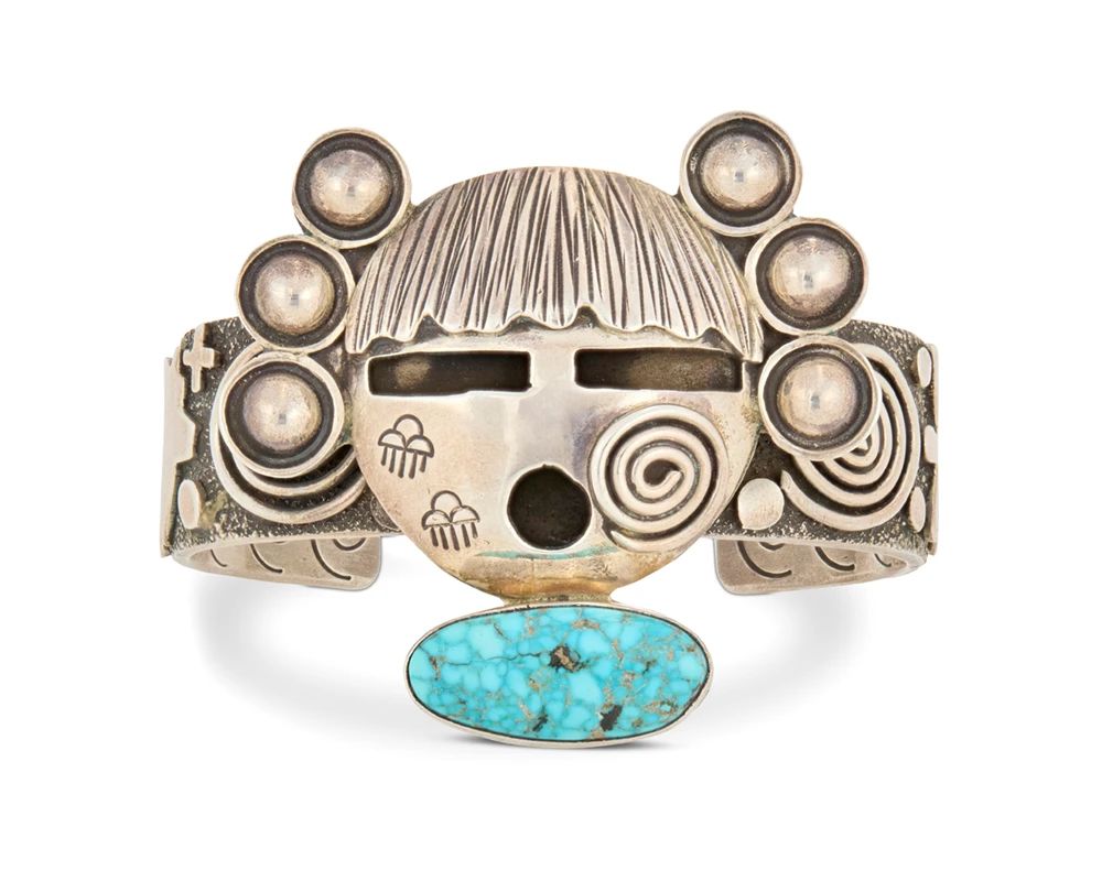 2001 An Alex Sanchez Navajo sterling silver and turquoise cuff bracelet Alex Sanchez (b. 1967, Diné/Zuni) 21st century Stamped for artist and for sterling A chunky cuff featuring a central sculptural Katsina mask and set turquoise, with applied silver petroglyph and bear motifs to band and stampwork to interior 6.5" total inner C x 2" H, gap: 1.25" 102.8 grams gross Estimate: $700 - $800