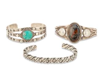 2262 A group of Southwest style sterling silver cuff bracelets Early/mid-20th century Each unmarked Three works comprising a Fred Harvey style three wire cuff with set turquoise and stampwork, a two wire cuff with set petrified wood cabochon and stampwork, and a narrow twisted wire cuff 3 pieces Largest: 6.625" total inner C x 0.25" H, gap: 1.375"; Smallest: 6" total inner C x 0.875" H, gap: 0.75" 79.7 grams gross Estimate: $200 - $400