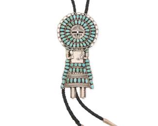 2086 A Larry Moses Begay Navajo cluster set kachina bolo Larry Moses Begay (b. 20th century, Diné) Late 20th century Stamped: LMB / Sterling A large sterling silver sculptural bolo of a standing Sunface katsina figure with elaborate cluster set turquoise, set to a black braided leather cord with silver cone and ball tips Bolo slide: 5.375" H x 2.625" W; cord: 37" L 93.0 grams gross Estimate: $400 - $600