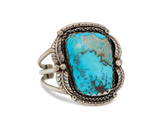 2004 A large Southwest sterling silver and turquoise cuff bracelet Mid/late 20th century Stamped to terminal: GM [possibly Gerald Mitchell, Navajo/Diné] A chunky three wire silver cuff with a set slab turquoise and multiple applied silver feather accents 6.5 total inner C x 2.625" H, gap: 1" 102.8 grams gross Estimate: $500 - $700