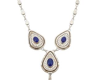 2075 A large Jonathan Nez Navajo sterling silver and lapis lazuli necklace Jonathan Nez (b. 1965, Diné) Late 20th/21st century Etched signature: Jonathan Nez; Sterling A chunky link necklace with three incised sterling silver teardrop bolo style plaques, each with a central set lapis lazuli cabochon, the center plaque with two silver dangles, all suspended from a paperclip style chain with alternating silver dot links 27.5" L x 5.5" H 297.6 grams gross Estimate: $800 - $1,200