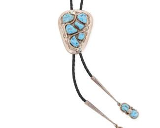 2078 An Effie Calavaza Zuni sterling silver and turquoise bolo tie Effie Calavaza (1927-2019, Zuni Pueblo) Late 20th/21st century Stamped: Effie C. / Zuni A trapezoidal sterling silver and turquoise serpent bolo with set nugget turquoise and applied silver serpents suspended on a black braided leather strap with tapered silver tips and serpent turquoise dangles Bolo slide: 2.75" H x 2.125" W; cord 40" L 80.0 grams gross Estimate: $400 - $600