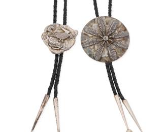2247 Two Southwest sterling silver bolo ties Late 20th century One etched: Ron Davis / Sterling Comprising a Ron Davis large silver disc bolo with applied feather motifs, as well as a silver nugget bolo with applied silver pictograph motifs, each on a braided black leather cord with silver tips 2 pieces Bolo slides: 2.625" Dia. and 1.625" H x 1.75" W; cords: 38" L approximately 100.8 grams gross Estimate: $200 - $400