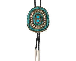 2084 A Zuni Pueblo style needlepoint bolo tie Mid/late 20th century Unmarked An oval plaque bolo with cluster set needlepoint turquoise on a braided black leather cord with silver metal cone tips Bolo slide: 3" H x 2.75" W; cord: 37" L 59.6 grams gross Estimate: $300 - $500