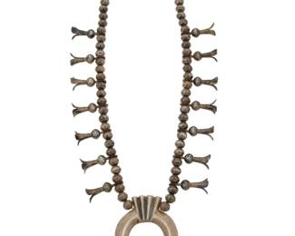 2122 A Southwest sterling silver squash blossom necklace Early 20th century Unmarked A heavy single strand of sterling silver beads and fourteen blossoms suspending a large sandcast sterling silver naja 25" L x 3" H 201.2 grams gross Estimate: $700 - $900