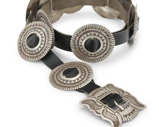 2095 A Navajo sterling silver concho belt Late 20th century, Diné Buckle with etched signature: Morgan [possibly Harry Morgan, 1946-2007, Diné] / Navajo; stamped: Sterling Comprising a rectangular sterling silver buckle and eleven round conchos, each with elaborate stampwork, and all mounted to a black leather belt strap Buckle: 1.625" H x 2" W; Each concho: 1.5" H x 1.875" W; Belt: 36.5" L x 0.75" H 328.1 grams gross Estimate: $800 - $1,200
