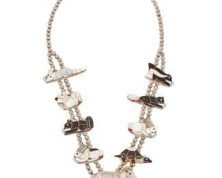 2116 An Ann Sheyka Zuni Pueblo sterling silver and stone inlay pictorial necklace Ann Sheyka (b. 1943-d., Zuni Pueblo) Marked: A. Sheyka [inscribed] A squash blossom-style animal fetish necklace, with eight detailed multi-stone inlay animal 'blossoms', including an armadillo, a grey squirrel, a black squirrel, two rabbits, a turtle, a beaver, and a skunk, as well as a large wolf 'naja' pendant to the center, worked in various stones including mother of pearl, turquoise, coral, and onyx/jet, all mounted on a double strand of silver beads and with a tapered silver cone clasp 27" L x 2" H 94.1 grams gross Estimate: $2,000 - $4,000