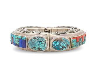 2012 A Hank Whitethorne Navajo large silver and cobblestone bracelet Hank Whitethorne (b. 20th century, Diné) Late 20th/21st century With etched signatures to interior A heavy chunky hinged bangle bracelet with set turquoise cabochons to terminals, with turquoise, coral, and lapis lazuli cobblestone inlay to band, and incised silver stepped hooked motif banding to each side 6.75" total inner C x 1.125" H x 1" D 217.1 grams gross Estimate: $800 - $1,200