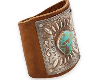 2046 A Navajo sterling silver and turquoise ketoh arm guard Mid-20th century, Diné Appears unmarked A rectangular repoussé stamped plaque with central set turquoise, and attached with rivets to a shaped brown leather arm band with snap fasteners Silver: 3" H x 2.75" W; Band: 3.5" H x 8.75" W 86.9 grams gross Estimate: $400 - $600