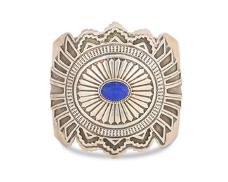 2026 A Gary Reeves Navajo sterling silver and lapis lazuli cuff bracelet Gary Reeves (1962-2014, Diné) Late 20th/21st century Stamped: G. Reeves; etched: Sterling A large wide concho-style cuff with elaborate chased silver overlay, central set lapis cabochon, and stamped terminals 7.375" total inner C x 2.875", gap: 1.375" 141.1 grams gross Estimate: $600 - $800