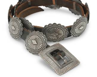 2098 A Daniel 'Sunshine' Reeves Navajo sterling silver concho belt Daniel 'Sunshine' Reeves (b. 1966, Diné) Late 20th century Stamped: Sunshine Reeves / Sterling Comprising fourteen oval conchos and a matching rectangular buckle, each with deep stampwork and overlay designs, and all mounted to a leather belt strap Buckle: 2" H x 2.5" W; Each concho: 1.875" H x 2.125" W; Belt: 48" L x 0.75" H 374.8 grams gross Estimate: $700 - $900