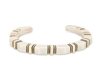 2032 A Nusie Henry Belon Navajo sterling silver and 14K gold cuff bracelet Nusie Henry [Belon] (b. 20th century, Diné) Late 20th century Stamped: Nusie / 14K / Sterling A narrow modernist style angled cuff with incised banding and 14K overlay details 6.125" total inner C x 0.25" H, gap: 1" 44.2 grams gross Estimate: $300 - $500