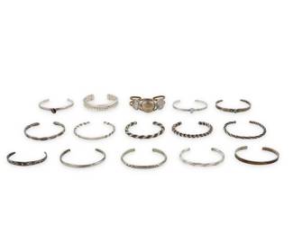 2292 A large group of Southwest style silver bracelets Mid/late 20th century Variously marked for maker and for sterling: K / DTr / LO [sun picto] A group of narrow silver wire cuffs in various styles and sizes, including twisted rope wire, stampwork, set stones including turquoise, purple cat's eye, and opal, as well as one with set coins, and one with 12K gold filled overlay 15 pieces Largest: 6.625" inner C; Smallest: 5.625" inner C 255.6 grams gross Estimate: $200 - $400