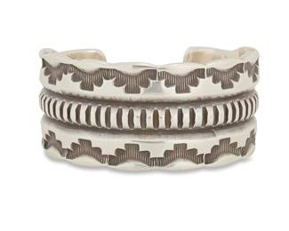 2028 An Emerson Bill Navajo sterling silver cuff bracelet Emerson Bill (b. 20th century, Diné) Mid/late 20th century Stamped: Emerson [script] / Sterling A chunky heavy gauge cuff with deep stampwork and ridged center band 6.5" total inner C x 1.25" H, gap: 1" 158.2 grams Estimate: $400 - $600