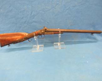 Lot 21. Antique double-barrel muzzle-loading coach shotgun from the mid to late 1800s. Fish scale hand grips with a hand-carved red stag embellishment on the stock. Both hammers in operating condition. Small wood loss to the front of the forearm. Original sling swivels. No FFL paperwork required.