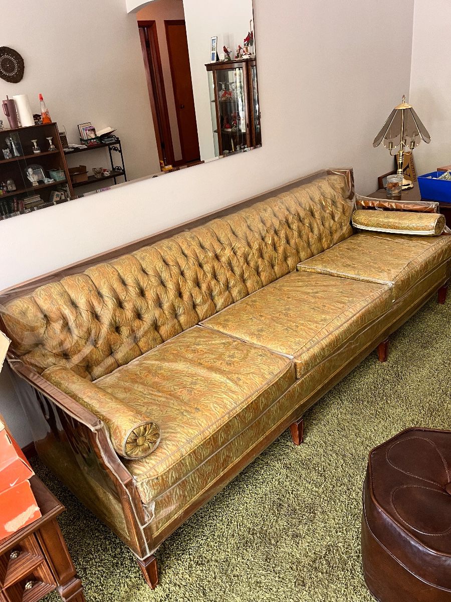 vintage Chesterfield-style sofa features button-tufted gold velvet upholstery and decorative wood accents still has plastic