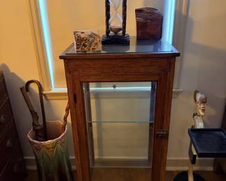 Narrow glass-front curio or storage cabinet with small tabletop items nearby.