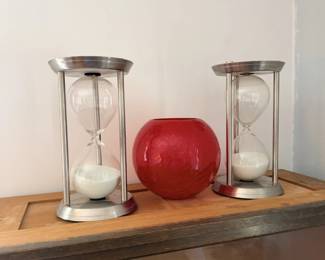 Pair of modern hourglass timers with red glass sphere on wood shelf.