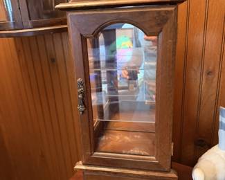 Slender glass-front curio cabinet with arched pediment, mirrored back and carved wood trim.