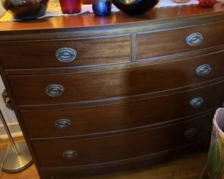 Wood chest/dresser with drawers, topped with colorful art-glass and pottery display pieces.