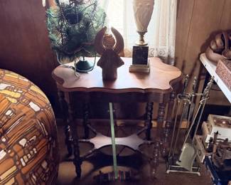 Round side table with lamp, art glass, plant decor, chair and woven baskets nearby.