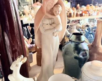 Tall pink Madonna or robed woman figure with white deer/swan nearby.