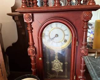 Ornate wood mantel or shelf clock with turned spindle gallery, Roman numeral dial and decorative brass-tone pendulum.