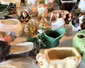 Close tabletop grouping with ceramic planters, figures, animal decor, colored pottery and small collector pieces.