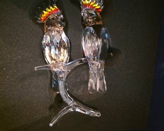 This Swarovski Crystal Paradise figurine, titled "Pink Cockatoos," features two detailed birds crafted from clear and pink crystal, perched on a crystal branch.