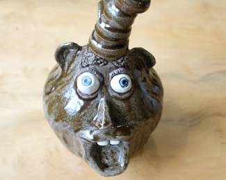 Up for sale is a highly collectible, authentic Southern folk art stoneware ceramic face jug handcrafted and signed by regional potter P. Hosey (Phillip Hosey) out of Carrollton, Georgia.This whimsical alkaline-glazed clay piece features an exceptionally unique, stylized smoking pipe or stack spout protruding from the top of the head, acting as a secondary vessel handle or opening. The figure displays classic "ugly face jug" characteristics, including prominent applied clay ears, wide white slip-trail eyes with cobalt blue pupils, and an open mouth showcasing individually sculpted white clay teeth.Perfect for collectors of traditional Georgia, North Carolina, and Edgefield-style pottery, outsider art, face vessels, and signed American studio stoneware.Artisan: Phillip "P." Hosey (Carrollton, GA)Material: Hand-thrown stoneware clay, glaze, slipCondition: Excellent vintage condition with no visible chips, cracks, or repairs.