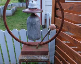 This metal garden bell sculpture features a large cylinder bell hanging inside a hoop design.