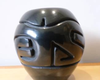 This blackware pottery jar is by artist Stella Chavarria of the Santa Clara Pueblo and features deeply carved geometric patterns.It is hand-coiled and stone-polished to a high sheen.The piece typically measures around 3.5 inches in height.It is signed on the bottom as "Stella Chavarria, Santa Clara Pueblo"