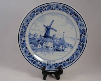 This Royal Delft wall plate is a blue and white ceramic piece featuring a traditional windmill and waterscene.