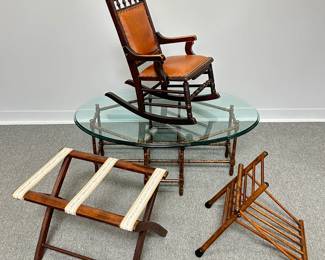 A child-sized handcrafted wooden rocking chair with inset barley twist supports and brown leather tack upholstered cushions; a vintage Baker Hollywood Regency era faux bamboo oval coffee table with a removable glass top on an octagonal, eight-legged faux bamboo base with a lacquered finish, 44” W x 31” D x 16” H; a vintage mahogany folding luggage rack with decorative tapestry straps; and a vintage wooden folding gout stool featuring spindle construction
