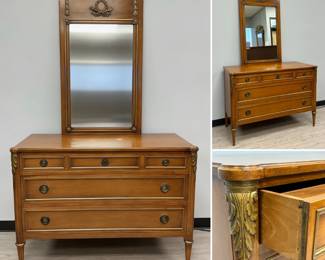 A low chest of drawers or commode crafted in a Directoire/Empire style, five drawers, Neoclassical details like fluted pilasters topped with gilded acanthus leaves, tapered feet, and brass mounts. 47”W x 21”D x 34”H. Shown with matching tall Trumeau style mirror resting on top of the dresser, the top with gilded carvings of a laurel wreath and torches; 27”W x 43”H.