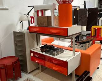 A Raymond Loewy DF2000 red two-drawer console with stand, a Raymond Loewy DF2000 series red four-drawer console with stand, and a Raymond Loewy DF 2000 dressing cabinet, "Valet 2000/50" designed by Raymond Loewy for Doubinsky Freres, circa 1969, this model in the Sepia color scheme; and Mid-century modern 1970s vintage magazine rack designed by Giotto Stoppino for Kartell, black plastic, manufactured in Italy