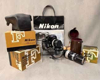 A vintage Nikon F Photomic FTN film camera in black with original box, a Nikon Eveready semi-soft leather camera case with original box, a vintage Nikon Nippon Kogaku NIKKOR-Q Auto 200mm f/4 telephoto lens with hardshell leather carrying case, a vintage Nikon Nikkor-Auto 35mm f/2 lens with original box, and Nikon store shopping bag.