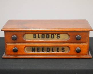 A late 19th century Blood's counter top sewing needles cabinet. Walnut construction features two labeled dovetailed drawers with two ebonized wood knobs each. Old refinish with wear with some nicks/losses. 17 1/4 x 9 1/4 x 6 1/4" high overall. ESTIMATE $200-300