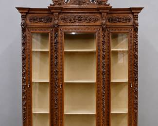 A late 19th century Victorian Period breakfront library case. Walnut construction with extensive hand carved detail features a carved crown with songbird, Stag head and floral swags over a molded crown and carved three panel frieze, over three doors with carved frames and beveled glass panels flanked by carved foliate columns and beveled glass side panels, on a stepped molded base with turned feet. Older refinishing with wear, one cracked side glass, minor damage, knocks down for transport. 74 x 23 1/2 x 137" high overall. ESTIMATE $2,000-3,000