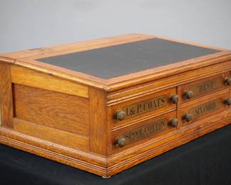 A turn of the century J. & P. Coats Counter Top Spool Cabinet. Oak construction features a lift up writing slope over four labeled dovetailed drawers with brass knobs along with an advertising panel featuring a large spool of thread verso. Old refinish with minor wear. 30 x 20 x 12" high. ESTIMATE $200-300